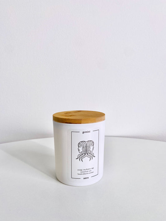 A Gemini candle, depicting two women's heads back-to-back, scented orange, eucalyptus and sage